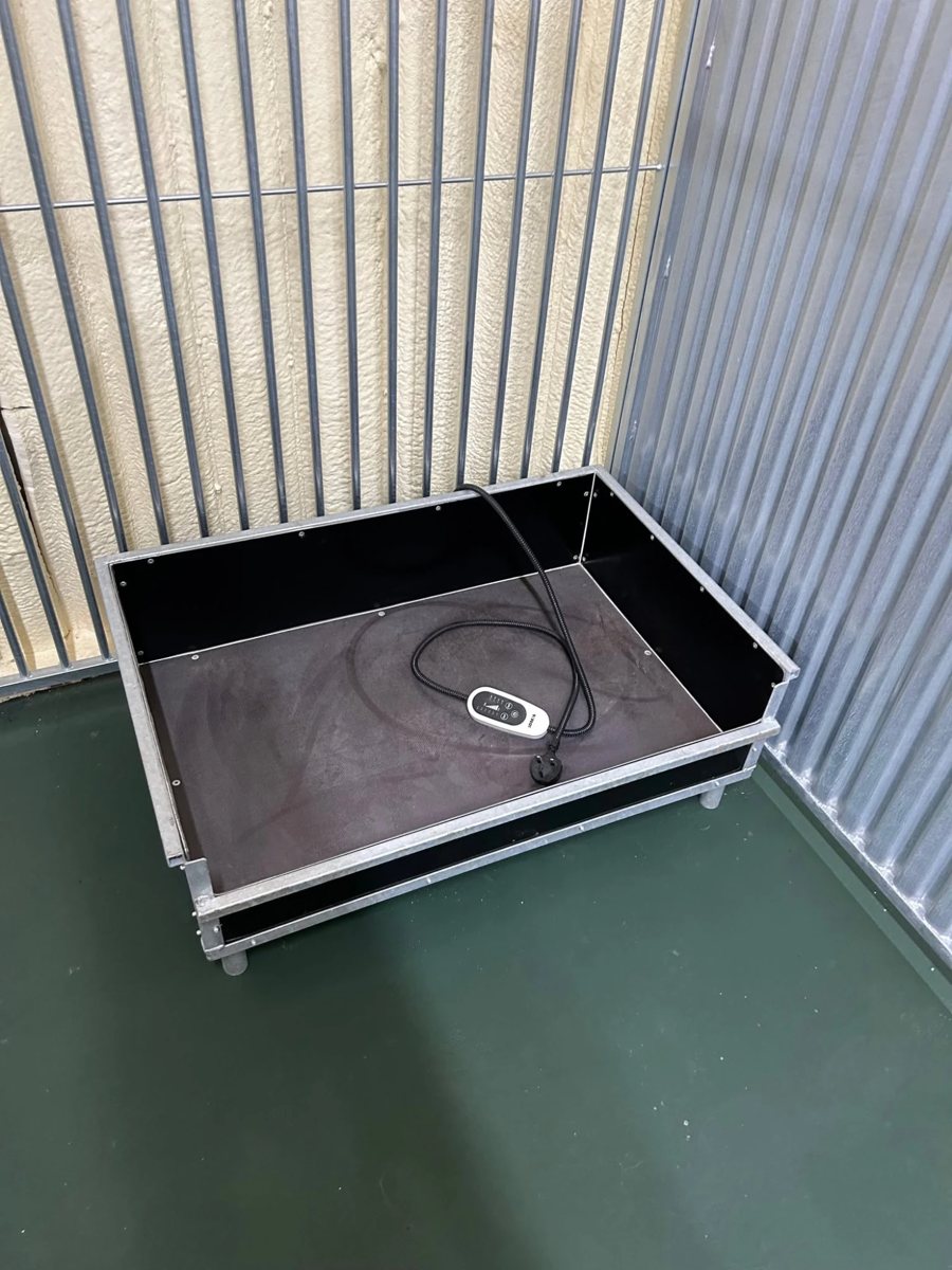 A raised kennel bed with its heating pad controller